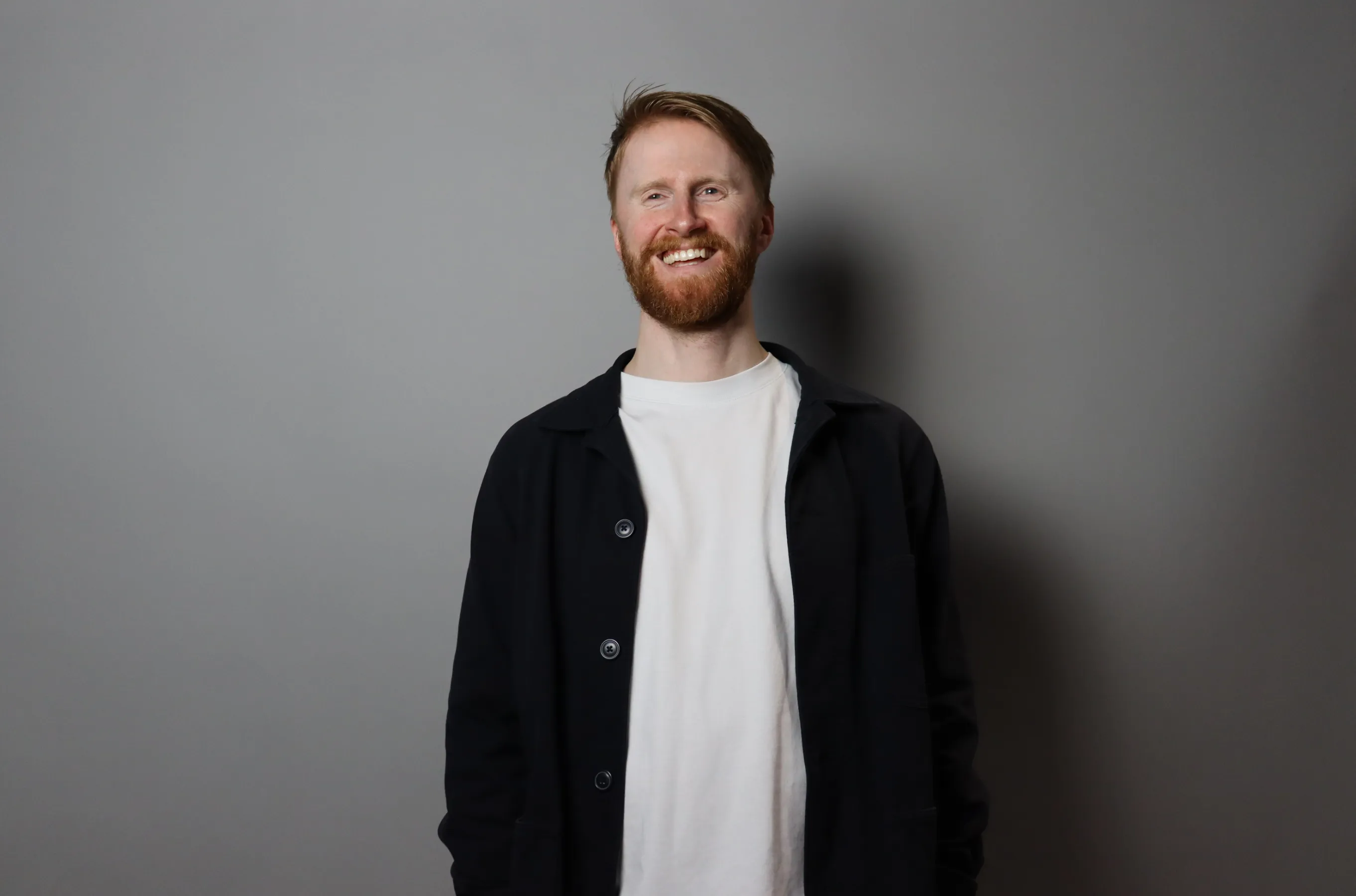 Chris Bullen laughing, standing against a grey wall